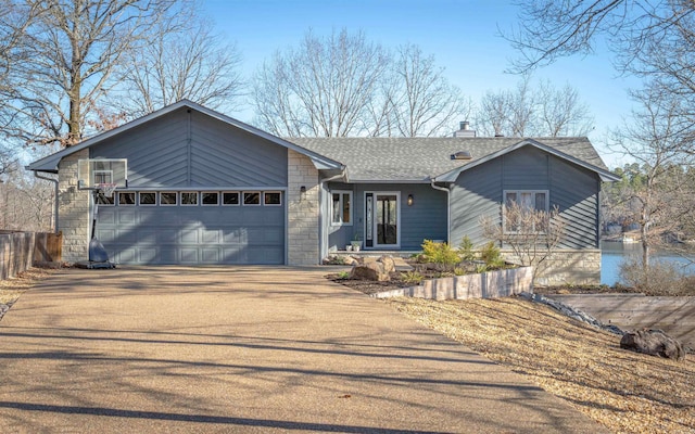 mid-century home featuring driveway, roof with shingles, an attached garage, a chimney, and stone siding