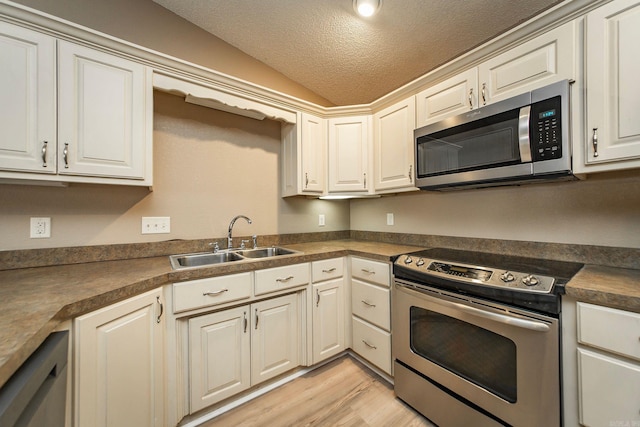 kitchen featuring light wood-style flooring, a sink, a textured ceiling, stainless steel appliances, and vaulted ceiling