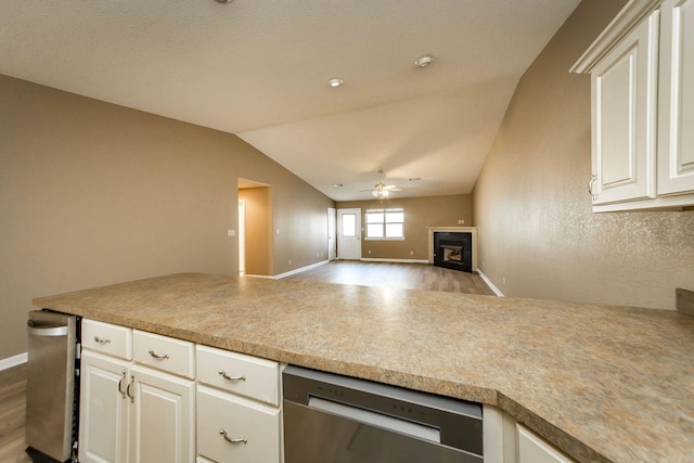 kitchen with stainless steel dishwasher, white cabinetry, a fireplace, lofted ceiling, and ceiling fan