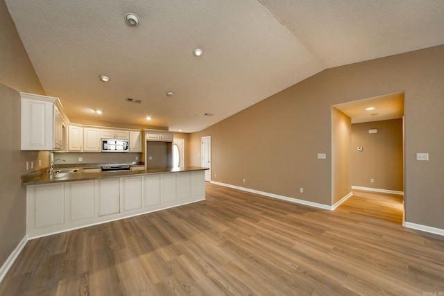 kitchen featuring a peninsula, a sink, vaulted ceiling, appliances with stainless steel finishes, and light wood-type flooring