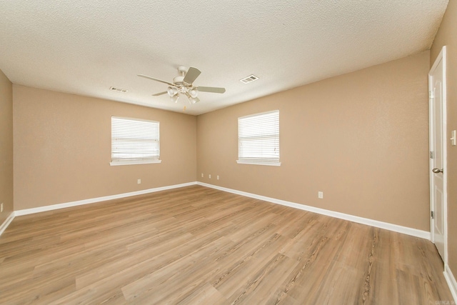 unfurnished room with a wealth of natural light, visible vents, light wood-style flooring, and a ceiling fan