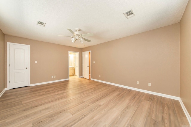 empty room with light wood-style floors, a ceiling fan, visible vents, and baseboards