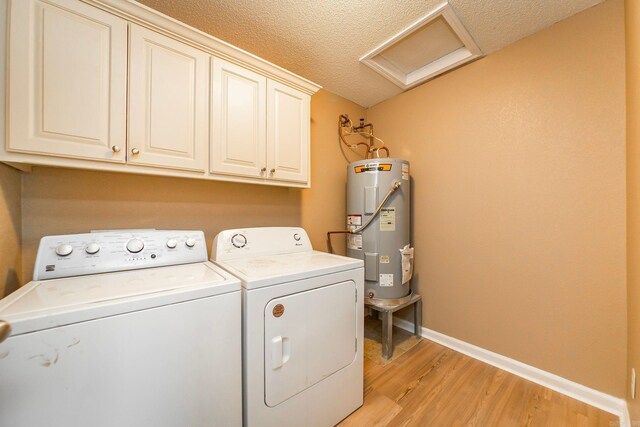 laundry area with washing machine and clothes dryer, light wood finished floors, electric water heater, attic access, and cabinet space