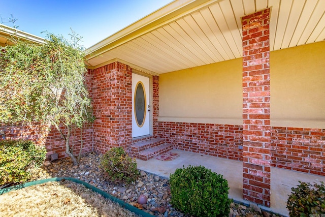 view of exterior entry featuring brick siding and stucco siding