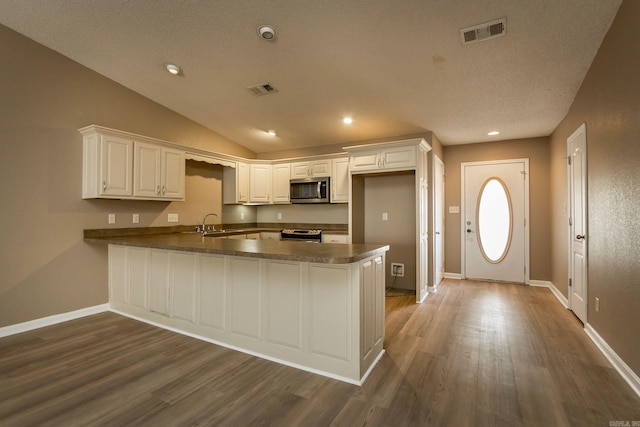 kitchen with stainless steel appliances, dark countertops, visible vents, and a peninsula