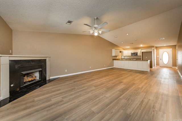 unfurnished living room with visible vents, a ceiling fan, light wood-style floors, and lofted ceiling