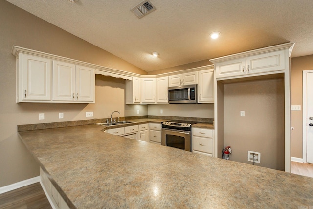 kitchen with visible vents, vaulted ceiling, a peninsula, stainless steel appliances, and a sink