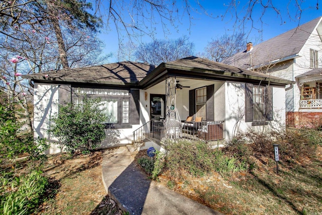 view of front of home with a shingled roof, a ceiling fan, covered porch, and stucco siding