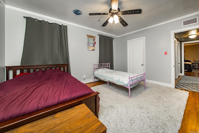 bedroom featuring baseboards, wood finished floors, visible vents, and ornamental molding