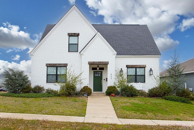 view of front of home featuring brick siding, a front lawn, and a shingled roof