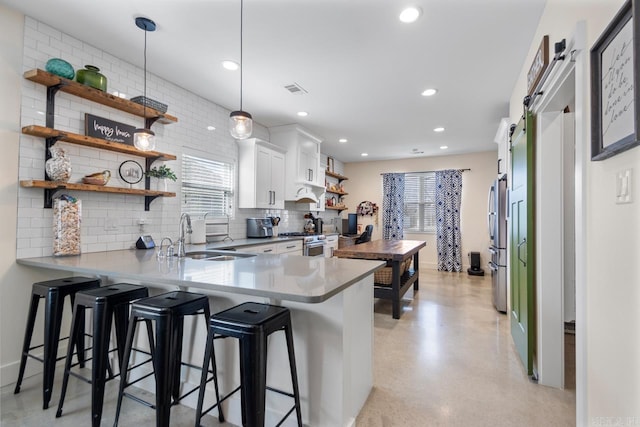 kitchen with open shelves, a kitchen bar, appliances with stainless steel finishes, and a sink