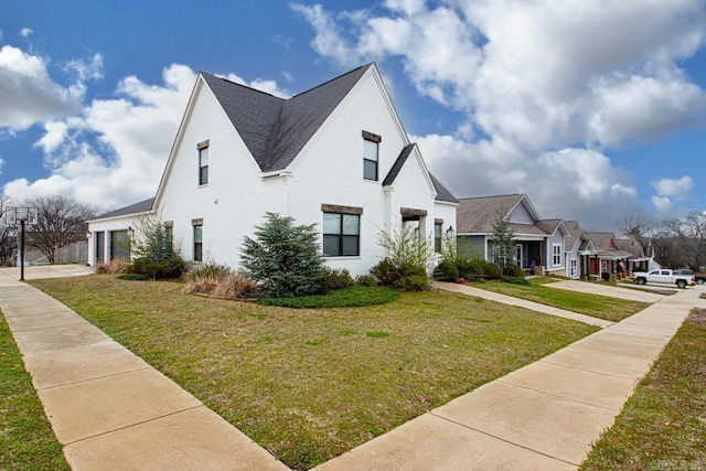 view of side of property featuring a lawn, driveway, a shingled roof, a garage, and brick siding