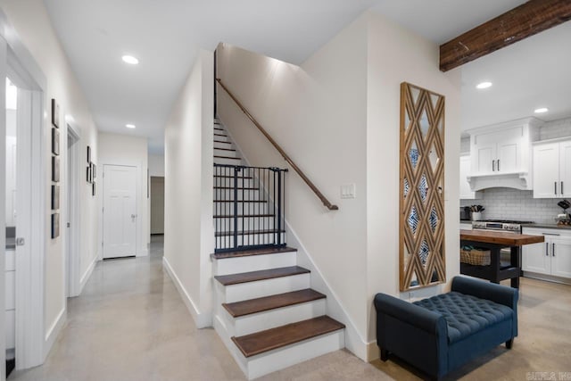 staircase with beam ceiling, recessed lighting, finished concrete flooring, and baseboards