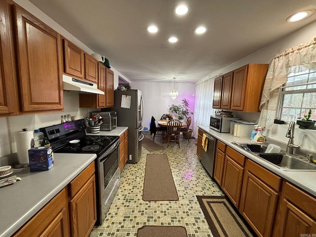 kitchen featuring under cabinet range hood, light countertops, appliances with stainless steel finishes, brown cabinetry, and a sink