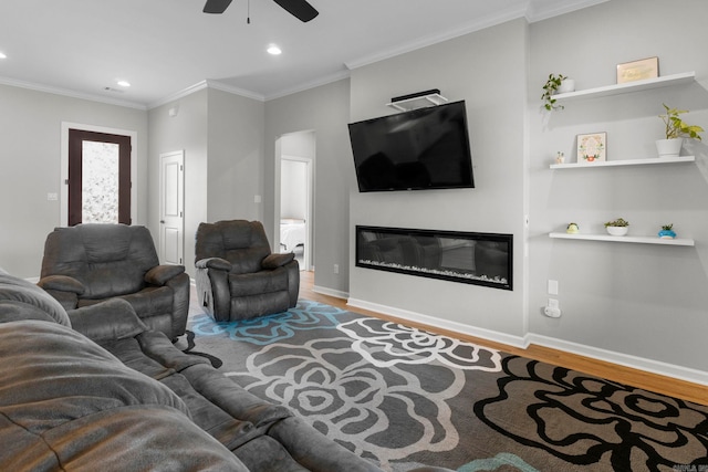 living area featuring a glass covered fireplace, ornamental molding, wood finished floors, and ceiling fan