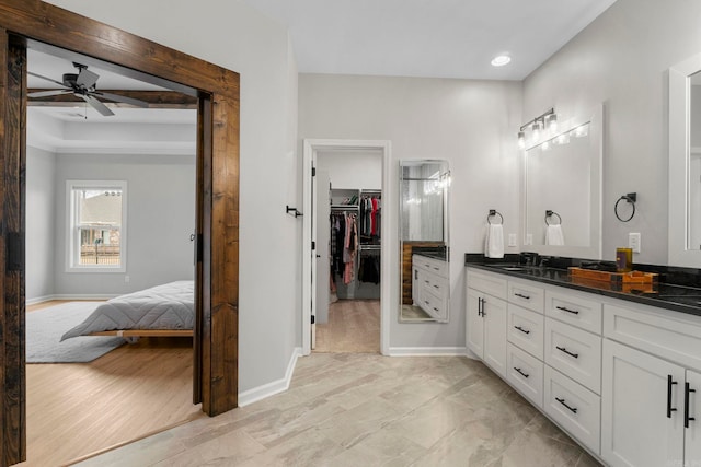 ensuite bathroom featuring baseboards, a ceiling fan, a spacious closet, and vanity