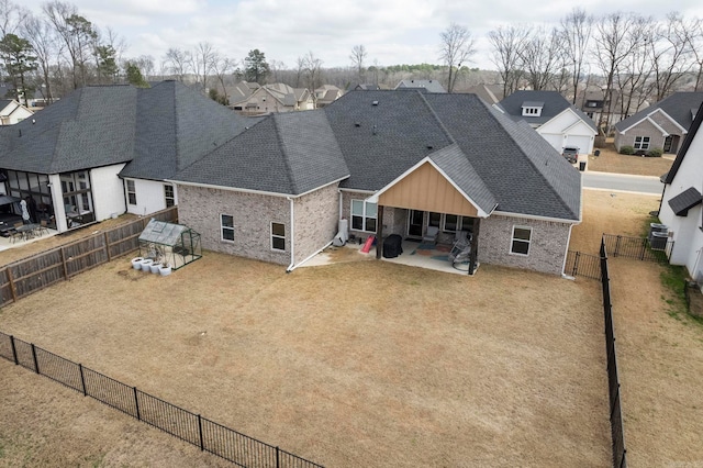 rear view of property with brick siding, a shingled roof, a residential view, a fenced backyard, and a patio