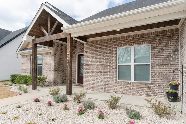 view of exterior entry featuring brick siding, a patio area, and roof with shingles