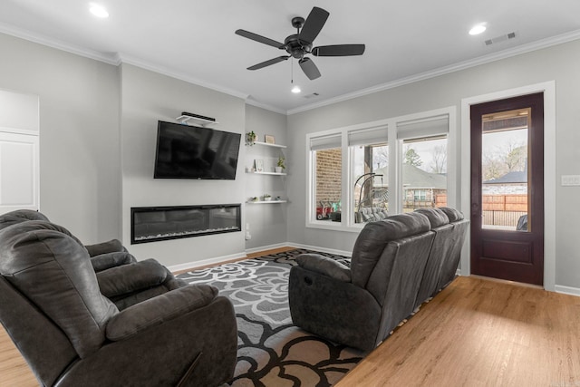 living area featuring visible vents, baseboards, ornamental molding, light wood-style flooring, and a glass covered fireplace