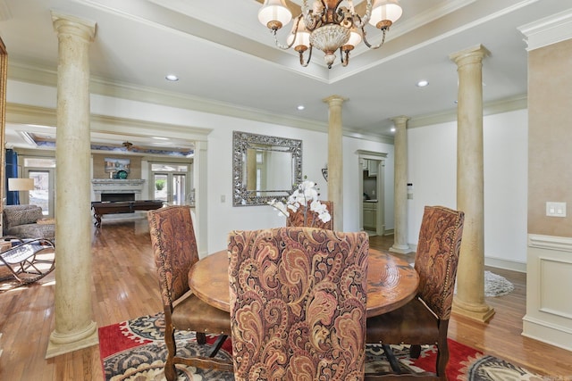 dining area with a tray ceiling, wood finished floors, crown molding, decorative columns, and a chandelier