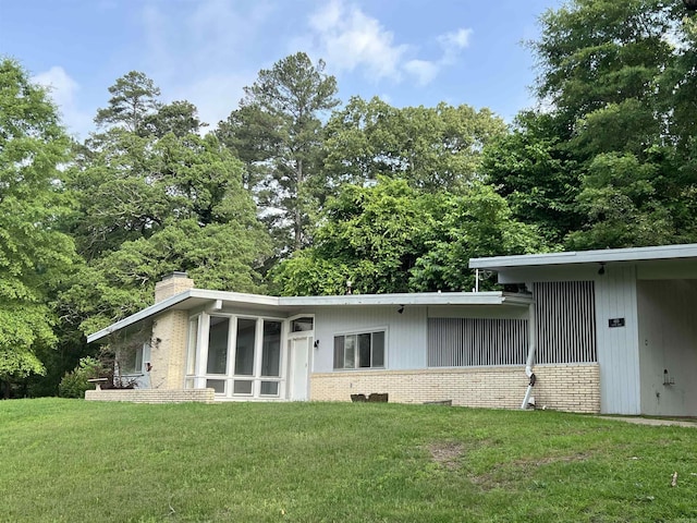 exterior space featuring brick siding, a lawn, a chimney, and a sunroom