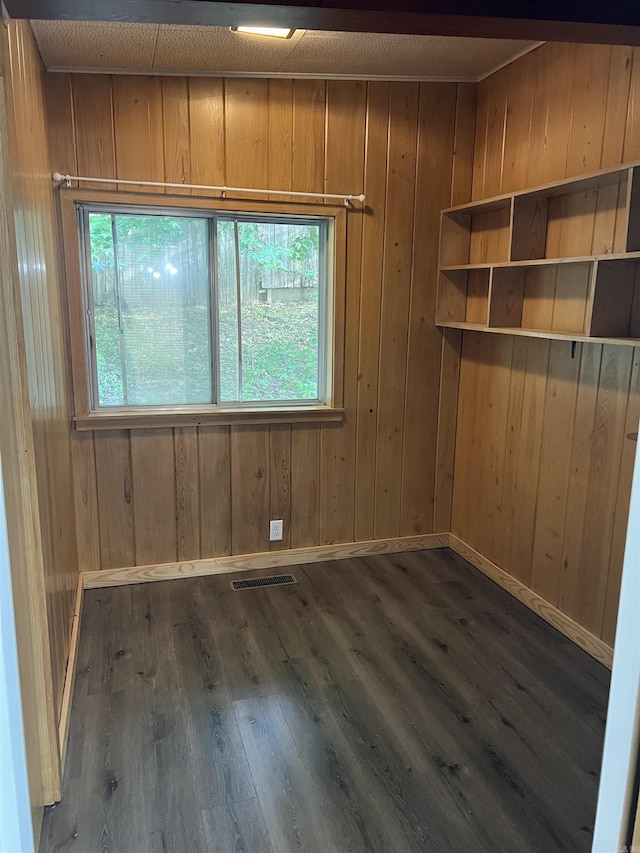 empty room with wooden walls, dark wood-style floors, visible vents, and baseboards