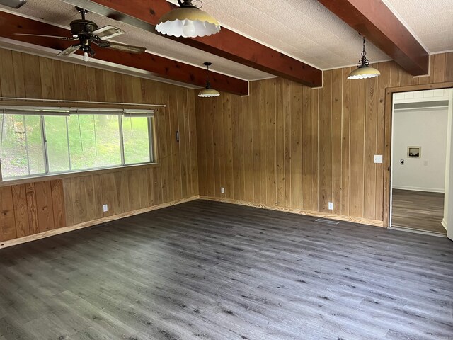 unfurnished room with baseboards, beamed ceiling, wood walls, wood finished floors, and a ceiling fan