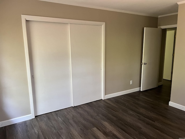 unfurnished bedroom featuring dark wood finished floors, a closet, baseboards, and ornamental molding