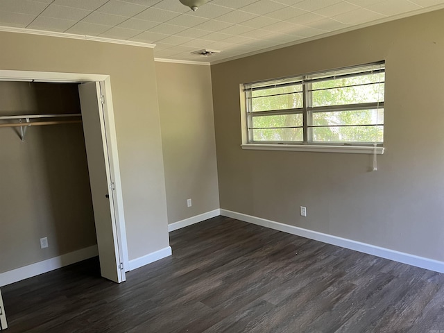 unfurnished bedroom featuring visible vents, baseboards, ornamental molding, dark wood-type flooring, and a closet