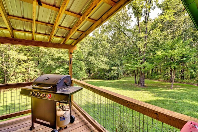 wooden deck with grilling area, a lawn, and a view of trees