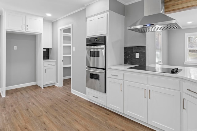 kitchen featuring tasteful backsplash, double oven, light wood-type flooring, white cabinetry, and wall chimney exhaust hood