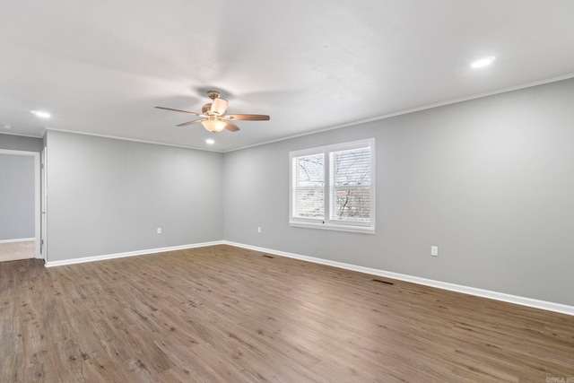 empty room with crown molding, wood finished floors, a ceiling fan, and baseboards