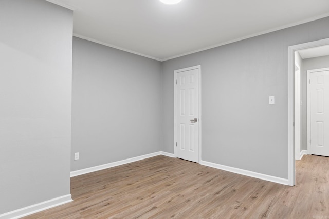 empty room featuring light wood-type flooring, baseboards, and crown molding