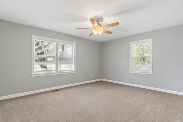 carpeted empty room featuring visible vents, baseboards, a healthy amount of sunlight, and a ceiling fan