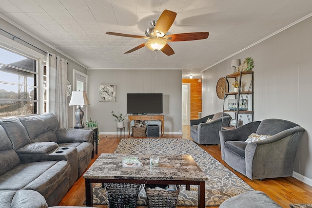 living area with crown molding, wood finished floors, baseboards, and ceiling fan