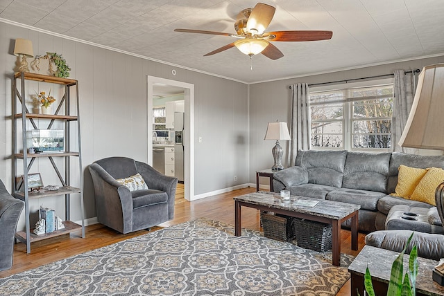 living room featuring baseboards, wood finished floors, a ceiling fan, and crown molding