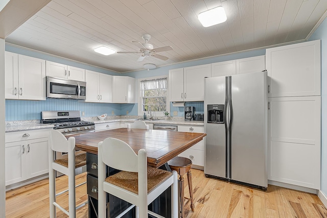 kitchen featuring ceiling fan, light wood-style floors, white cabinets, stainless steel appliances, and a sink