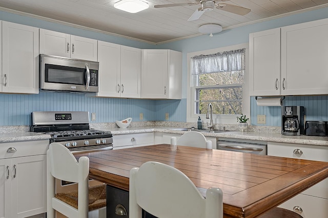 kitchen featuring crown molding, appliances with stainless steel finishes, white cabinetry, a ceiling fan, and a sink