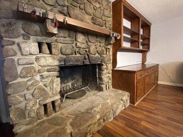 room details featuring a stone fireplace, wood finished floors, baseboards, and a textured ceiling