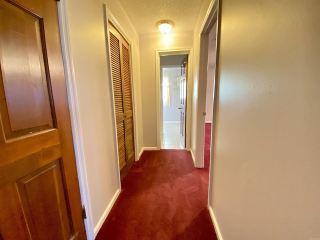 corridor featuring dark colored carpet, baseboards, and a textured ceiling