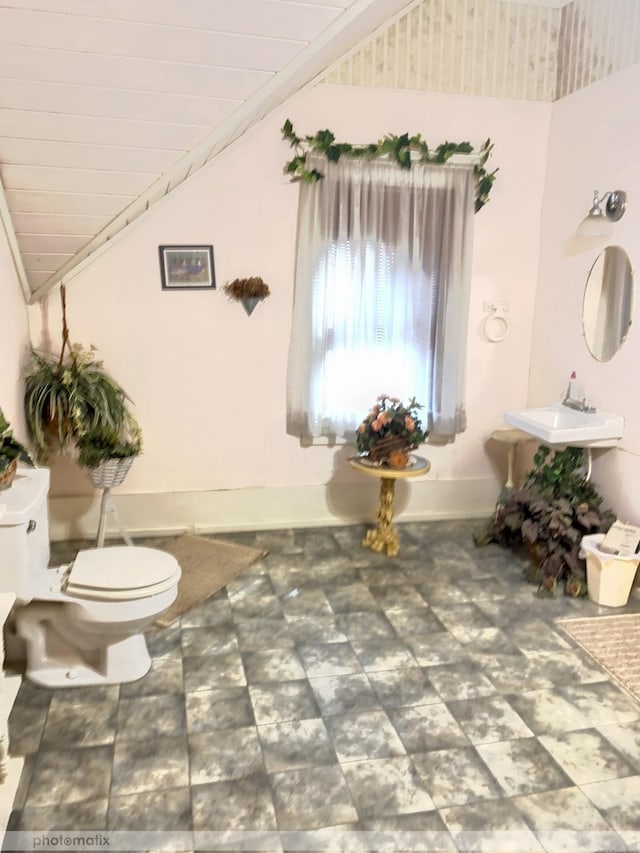 bathroom with lofted ceiling, toilet, baseboards, and a sink