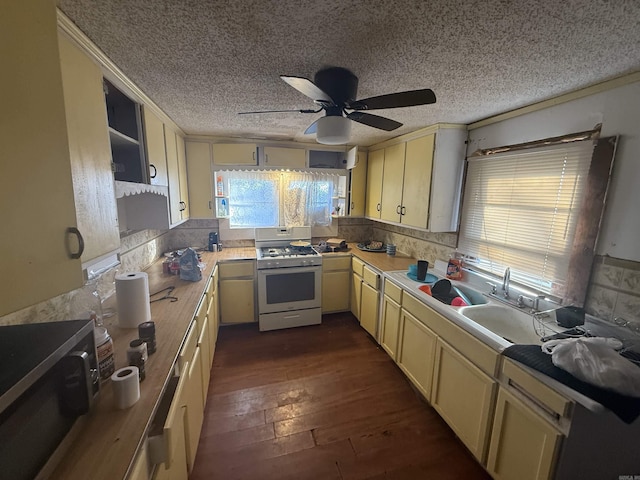 kitchen with stainless steel microwave, dark wood-type flooring, white gas range oven, a ceiling fan, and a sink