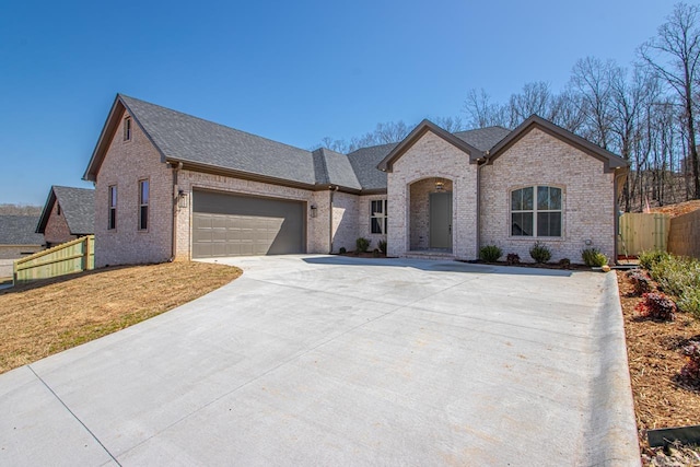 french provincial home with driveway, fence, an attached garage, a shingled roof, and brick siding