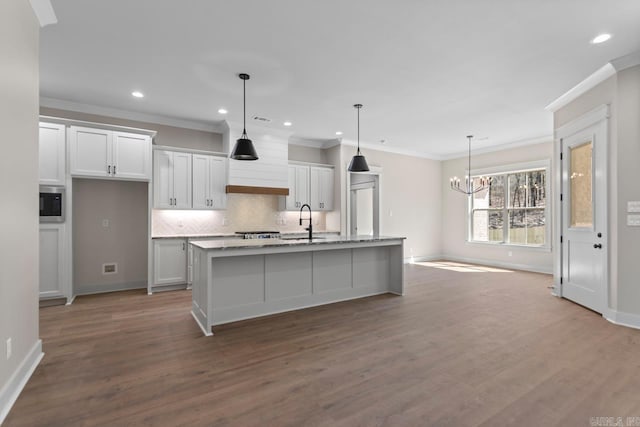 kitchen featuring a chandelier, a center island with sink, ornamental molding, decorative backsplash, and wood finished floors