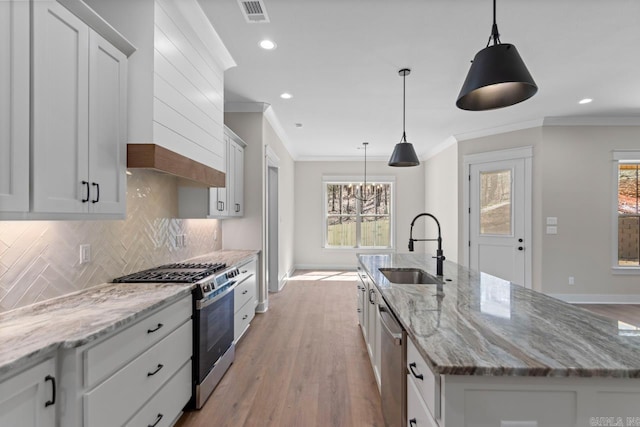 kitchen with premium range hood, a kitchen island with sink, a sink, appliances with stainless steel finishes, and backsplash