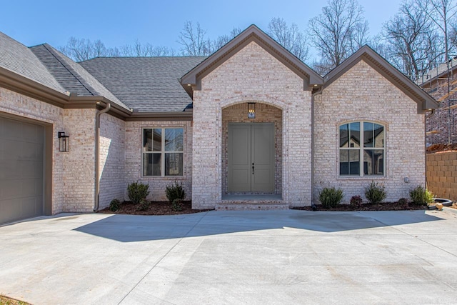 french provincial home with brick siding, concrete driveway, an attached garage, and a shingled roof