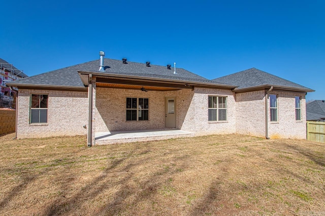 back of property featuring brick siding, fence, roof with shingles, a yard, and a patio area