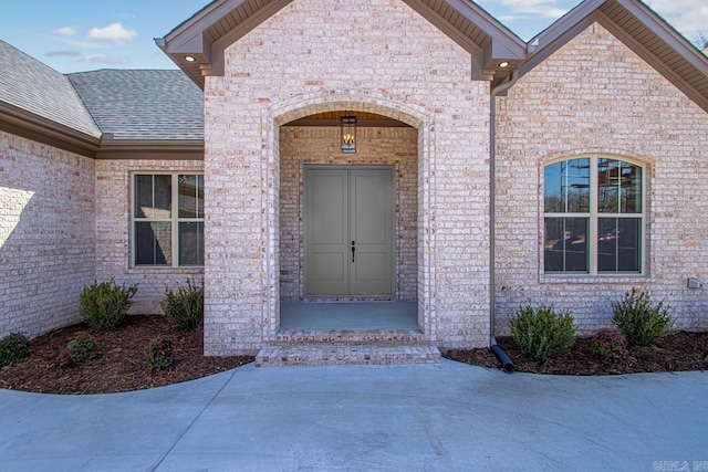 view of exterior entry with brick siding and a shingled roof