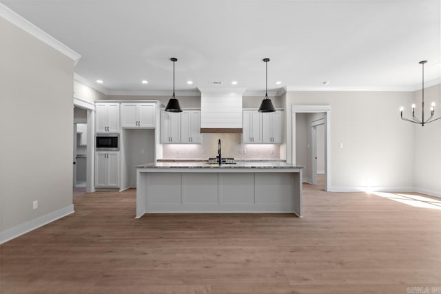 kitchen with light wood-type flooring, an island with sink, white cabinetry, stainless steel microwave, and tasteful backsplash