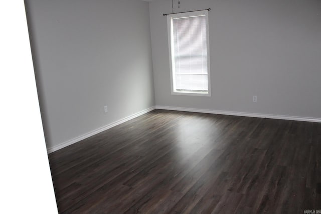 spare room with baseboards and dark wood-style flooring